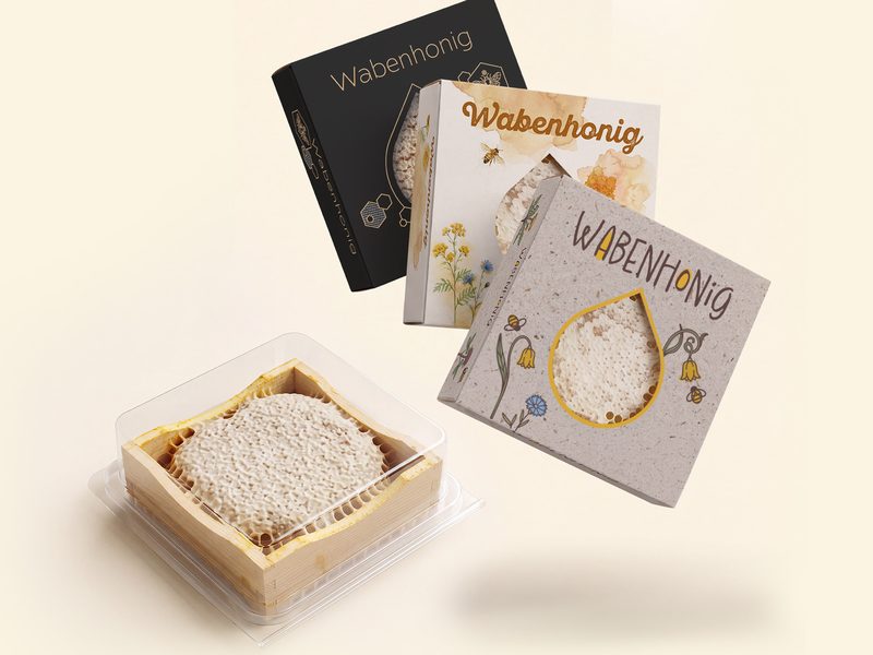 Drei Faltschachteln für Wabenhonig in verschiedenen Designs mit Sichtfenster und eine Aromabox mit Wabenhonigrähmchen